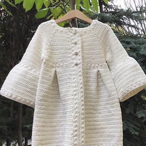 May include: A white crocheted cardigan with a button closure and bell sleeves.