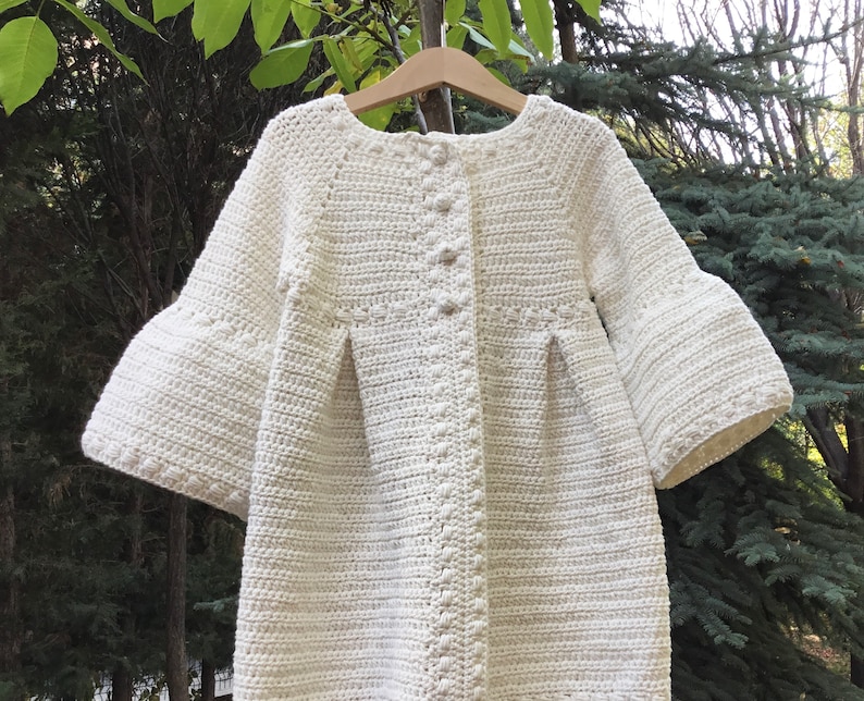 May include: A white crocheted cardigan with a button closure and bell sleeves.