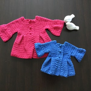 May include: Two crocheted baby cardigans, one pink and one blue, with a button closure and bell sleeves.