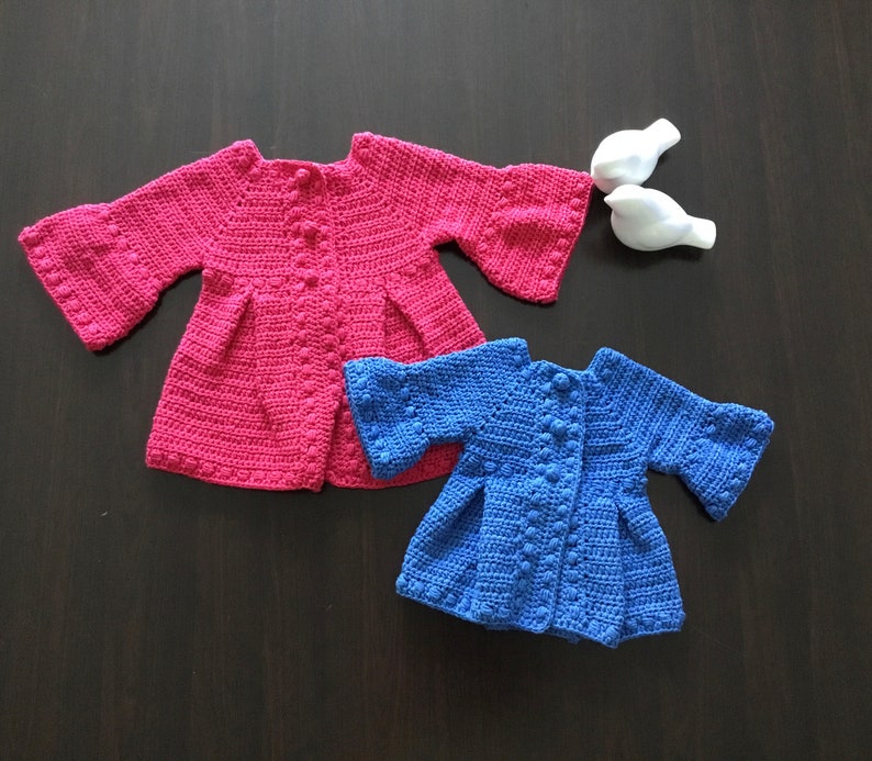 May include: Two crocheted baby cardigans, one pink and one blue, with a button closure and bell sleeves.