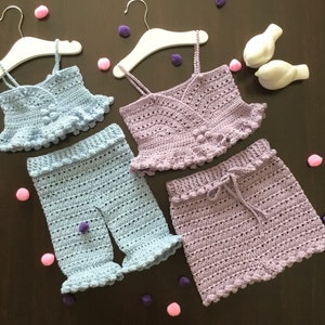 May include: Two crocheted baby outfits, one in light blue and one in lavender. Both outfits include a top with a ruffled hem and a pair of shorts.