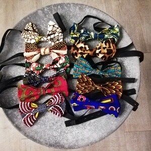 May include: A collection of ten bow ties with various colorful patterns and designs. The bow ties are arranged in a circle on a gray surface.