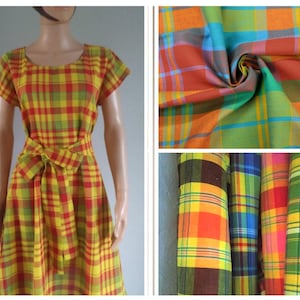 Peut inclure: Une robe à motif écossais vif dans des tons de jaune, rouge, orange, vert et bleu, avec des manches courtes, une encolure ronde et une ceinture en tissu assortie à la taille, présentée avec des échantillons de tissu pliés et roulés.