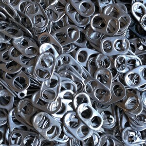 Peut inclure: Une image en gros plan d'un grand tas de tirettes argentées provenant de canettes de boissons en aluminium.