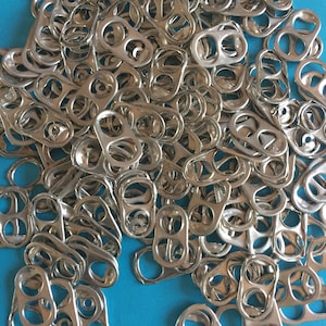 Peut inclure: Un tas de tirettes en argent provenant de canettes de boissons en aluminium sur un fond bleu vif.