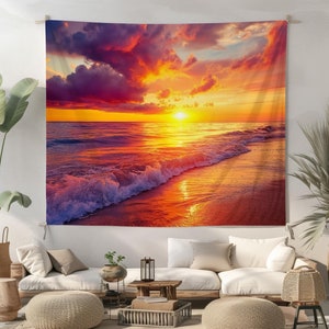 Op de afbeelding: Een wandkleed met een levendige zonsondergang boven een rustige oceaan met golven die de kust raken. De lucht is een mix van paars, oranje en geel, met pluizige wolken. Het water is diepblauw en reflecteert de kleuren van de lucht. Het strand is zandgeel, met een paar zichtbare voetafdrukken.