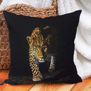 Op de afbeelding: Zwart kussen met een gouden en zwart luipaardprint. De luipaard kijkt naar voren met zijn hoofd naar beneden gekanteld.