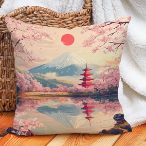 Könnte beinhalten: Ein Dekokissen mit japanisch inspiriertem Design, das eine rote Pagode, den Fuji, Kirschblüten und die Spiegelung der Szene in einem See zeigt. Das Kissen hat einen hellbeigen Hintergrund mit einer roten Sonne in der oberen rechten Ecke.