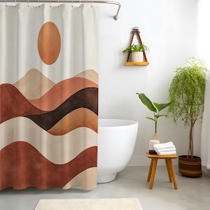 May include: A beige shower curtain featuring a watercolour design of a sun and layered mountain range in shades of brown, tan, and rust. The curtain hangs in front of a white bathtub. A small wooden stool holds towels and a vase with a plant.