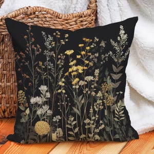 Op de afbeelding: Een zwart kussen met een bloemenprint met gedroogde bloemen in tinten geel en wit op een zwarte achtergrond.