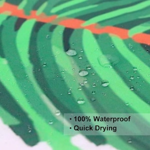 Puede incluir: Primer plano de una cortina de ducha de tela con estampado de hojas tropicales verdes y blancas. Hay gotas de agua en la tela, lo que demuestra las caracter&iacute;sticas impermeables y de secado r&aacute;pido de la cortina de ducha.