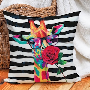 Pode incluir: Uma almofada colorida com um fundo de listras pretas e brancas apresenta uma girafa de óculos segurando uma rosa vermelha.
