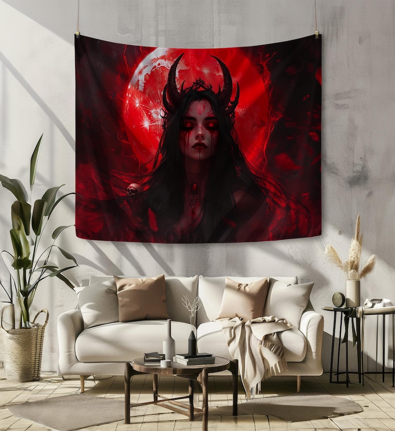 Peut inclure: Une tapisserie rouge et noire repr&eacute;sentant une figure d&eacute;moniaque avec des cornes et une couronne, sur fond de lune rouge. L'&oelig;uvre d'art a un th&egrave;me gothique, avec de longs cheveux noirs et des yeux rouges. La tapisserie est accroch&eacute;e au-dessus d'un canap&eacute; blanc.