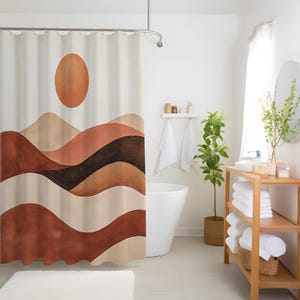 May include: A beige shower curtain with a landscape design featuring a brown sun and layered, wavy mountains in shades of brown and beige. The curtain hangs from a silver rail in a bright bathroom setting.