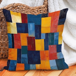 Könnte beinhalten: Ein farbenfrohes Kissen mit einem geometrischen Muster aus blauen, gelben, roten und orangen Quadraten. Das Kissen ist aus einem weichen, strukturierten Stoff gefertigt.