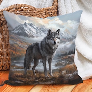 May include: A gray wolf with a white chest and a black nose stands in a snowy mountain landscape. The wolf is looking to the right of the image. The background is a misty mountain range with a blue sky and clouds.
