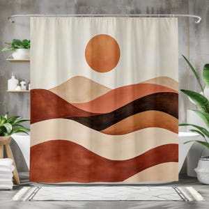 May include: A shower curtain with an abstract landscape design. The artwork shows rolling hills in shades of brown, beige, and black, with a large orange sun in the sky. The curtain hangs from a silver rail in a bathroom setting.