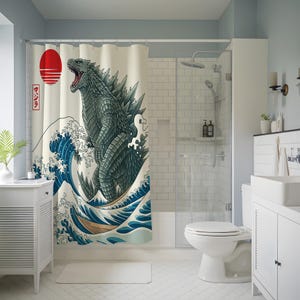 May include: A shower curtain featuring a Godzilla design in the style of a Japanese woodblock print. The artwork depicts Godzilla amidst a large ocean wave, with a red sun and Japanese text in the upper left corner. The color palette includes shades of blue, green, and beige.