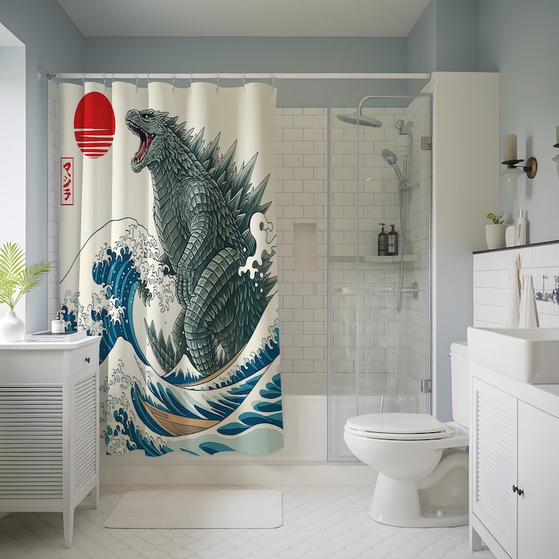 May include: A shower curtain featuring a Godzilla design in the style of a Japanese woodblock print. The artwork depicts Godzilla amidst a large ocean wave, with a red sun and Japanese text in the upper left corner. The color palette includes shades of blue, green, and beige.