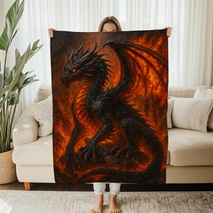 May include: A black dragon blanket with orange and red flames. The dragon has detailed scales, wings, and glowing orange eyes. The blanket is held up in front of a person.