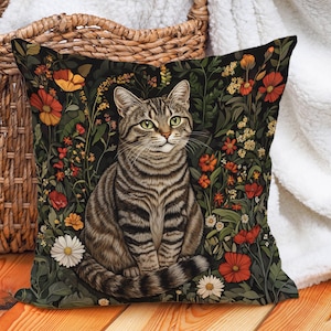 May include: A throw pillow with a black background featuring a tabby cat sitting in a field of colourful flowers. The cat has green eyes and a white patch on its chest.