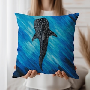 Könnte beinhalten: Quadratisches Kissen mit einem schwarz-weißen Walhai-Design vor blauem Hintergrund. Das Kissen hat ein strukturiertes Aussehen, wobei das Muster des Walhais und die Bewegung des Wassers detailliert dargestellt sind. Das Kissen wird von einer Person gehalten.