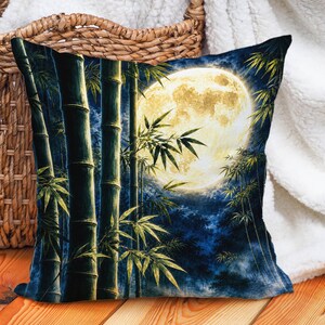 May include: A square throw pillow featuring a printed scene of dark green bamboo stalks in the foreground against a deep blue night sky. A large, bright yellow full moon illuminates the bamboo leaves and creates a contrast with the dark background.
