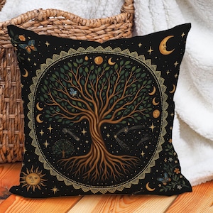 Puede incluir: Cojín decorativo negro con un diseño de árbol de la vida. El árbol es marrón con hojas verdes, rodeado de lunas, estrellas y un sol. El cojín tiene un borde dorado y detalles de mariposas, ideal para la decoración del hogar.