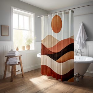 May include: A shower curtain featuring a watercolour design of a sun and layered mountain range in shades of brown, beige, and black. The curtain hangs in a bathroom with a white bathtub and wooden floor.