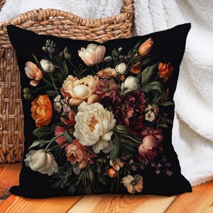 Può includere: Un cuscino nero con una stampa floreale che presenta una varietà di fiori in tonalità di rosa, rosso, bianco e arancio. I fiori sono disposti in un bouquet e sono posizionati su uno sfondo nero.