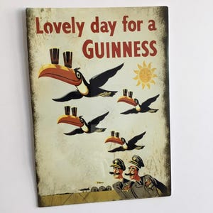 Puede incluir: Un letrero de estilo vintage con el texto "Lovely day for a Guinness". La imagen presenta tucanes de dibujos animados que llevan pintas de Guinness, un sol y dos hombres con uniformes militares. El letrero tiene un aspecto envejecido.