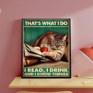 May include: A framed poster with a cat wearing glasses, reading a newspaper, and holding a glass of red wine. The poster has the text "THAT'S WHAT I DO, I READ, I DRINK AND I KNOW THINGS" in green and white.