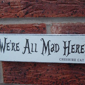 Verzerrtes Shabby Chic Schild „We're all mad here Grinsekatze Grinsekatze“.