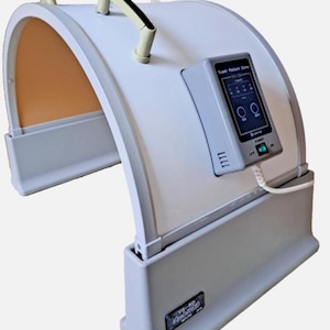 May include: A white and gray Super Radiant Dome sauna with a control panel displaying settings. The sauna has a curved design with a handle and a light tan interior. The control panel reads "Super Radiant Dome" and has an on/off switch.