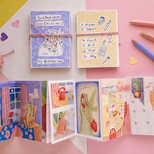 Può includere: Un piccolo libro illustrato colorato con una copertina blu e il testo "Folktale Week 2021 (15-21 Nov.) by @esther.bru". Il libro è aperto per rivelare illustrazioni di una casa, un telefono e una creatura verde. Il libro è su una superficie rosa con una superficie gialla dietro.