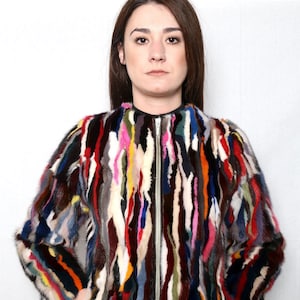 Puede incluir: Una chaqueta bomber de piel de colores con cierre de cremallera. La chaqueta está hecha de diferentes piezas de piel de colores cosidas juntas en un patrón de rayas.