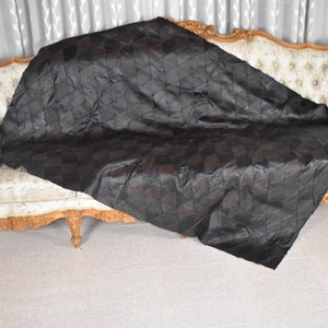 May include: A black leather throw blanket with a diamond pattern is draped over a light brown, ornate sofa with floral upholstery.