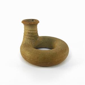 Può includere: Un piccolo vaso in ceramica di forma ad anello di colore marrone con un beccuccio. Il vaso è smaltato e ha un aspetto rustico.