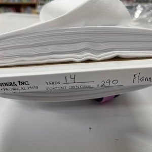 May include: White flannel fabric folded in a stack. The label reads "Fabric Finders, Inc." "530 Helton Dr. Florence, AL 35630" "Yards 14" "Content 100% Cotton" "#290 Flannel"