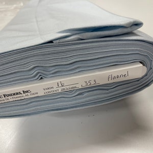 May include: A roll of light blue flannel fabric with a white label that reads "FABRIC FINDERS, INC. 4530 Helton Dr. Florence, AL 35630 YARDS 16 CONTENT 100% Cotton 353 Flannel"
