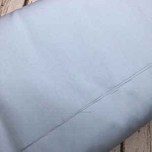 Pu&ograve; includere: Un tessuto blu chiaro con una texture sottile. Il tessuto &egrave; piegato a met&agrave; e i bordi sono visibili.