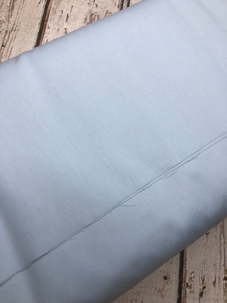 Pu&ograve; includere: Un tessuto blu chiaro con una texture sottile. Il tessuto &egrave; piegato a met&agrave; e i bordi sono visibili.