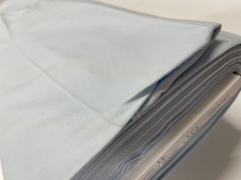May include: A stack of light blue flannel fabric. The fabric is folded and labeled "Flannel" with the text "Yards 1 1/2  100% Cotton 45.5"