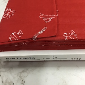 May include: Red fabric with a white repeating pattern of a cartoon car. The fabric is folded and labeled with "FABRIC FINDERS, INC." "P.O. Box 999 Florence, AL 35631-099" "YARDS 16" "CONTENT 100% Cotton" "#2128"