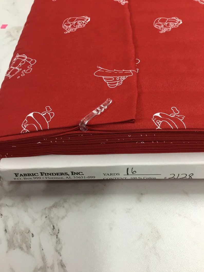 May include: Red fabric with a white repeating pattern of a cartoon car. The fabric is folded and labeled with "FABRIC FINDERS, INC." "P.O. Box 999 Florence, AL 35631-099" "YARDS 16" "CONTENT 100% Cotton" "#2128"