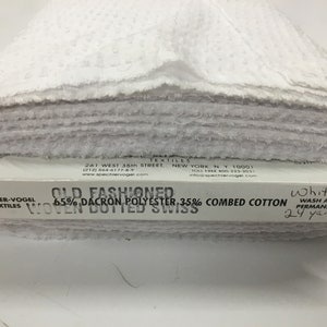 May include: White woven dotted swiss fabric roll, labeled "Old Fashioned 65% Dacron Polyester 35% Combed Cotton Woven Dotted Swiss" and "White Wash and Wear Permanent Press 24 yards".