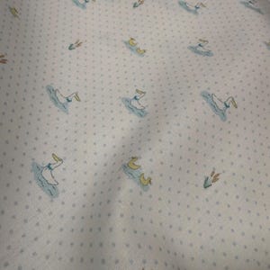 May include: White fabric with a repeating pattern of ducks swimming in blue water, with yellow beaks and accents. The fabric also features small, evenly spaced gray polka dots and green cattails.