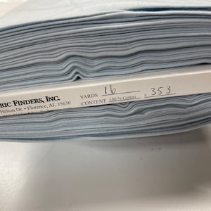 May include: A stack of light blue fabric with a white label that reads "FABRIC FINDERS, INC. 4530 Helton Dr. Florence, AL 35630 YARDS 16 CONTENT 100% Cotton # 353"