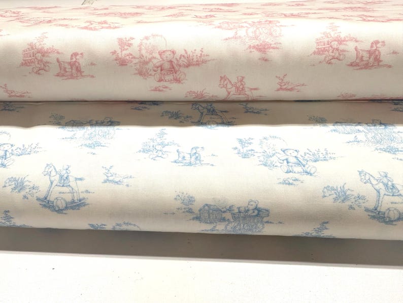 May include: Two rolls of fabric with a toile pattern. The top roll features a pink design with teddy bears and children on rocking horses. The bottom roll has a blue design with similar imagery. Both rolls are on a white background.