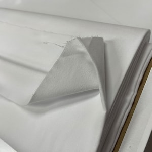 Op de afbeelding: Witte stof gevouwen in een stapel, wat de gladde textuur van het materiaal laat zien.